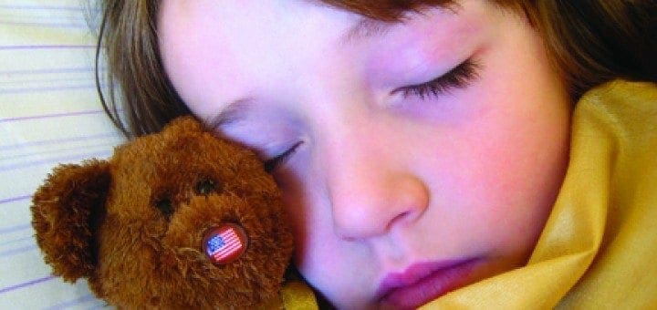 A young girl sleeps peacefully with her teddy bear tucked beside her.