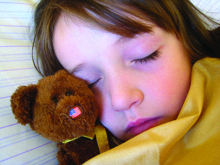 A young girl sleeps peacefully with her teddy bear tucked beside her.