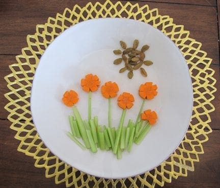 Carrot flowers and celery grass with a raisin sun on a white plate.