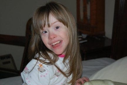 Young girl with Down syndrome smiles from a bed.