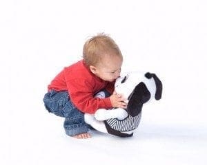 A toddler hugs a stuffed dog with black and white spots.