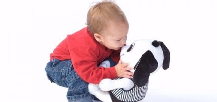 A toddler hugs a stuffed dog with black and white spots.