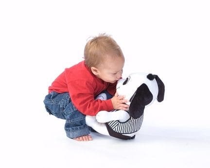 A toddler hugs a stuffed dog with black and white spots.