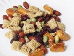 A pile of trail mix containing cereal squares, almonds, pretzels, raisins, cranberries, and edamame.
