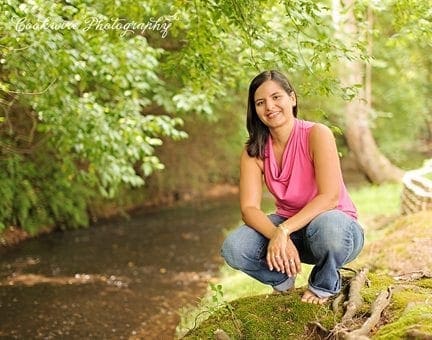 Sarah Cook, a photographer, crouches by a stream in a wooded area.