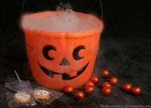 A jack-o'-lantern bucket filled with dry ice sits among Halloween candy and spiderwebs.