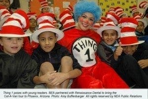 A woman dressed as Thing 1 smiles with children wearing red and white striped hats.