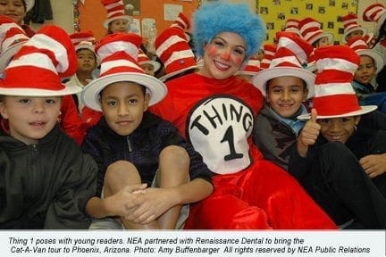 A woman dressed as Thing 1 smiles with children wearing red and white striped hats.