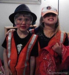 Two children dressed as construction workers wear orange safety vests and hats.