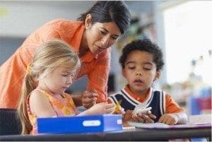 Teacher assists two young children with a lesson at a table.