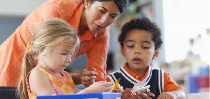 Teacher assists two young children with a lesson at a table.