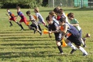 Children run a race on a grassy field holding orange cones.