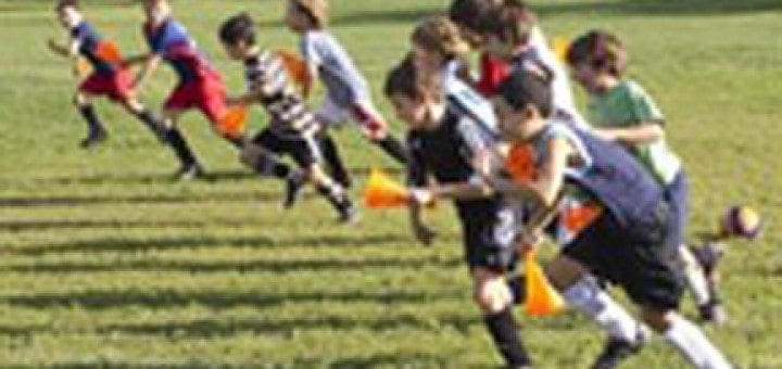 Children run a race on a grassy field holding orange cones.