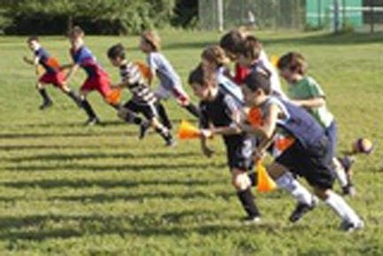 Children run a race on a grassy field holding orange cones.