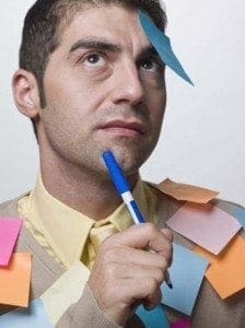 Man covered in sticky notes holds a marker while looking thoughtful.