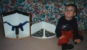 Child with glasses smiles next to custom-made corner chairs for adapted equipment.