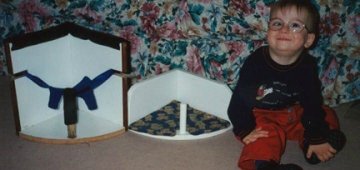 Child with glasses smiles next to custom-made corner chairs for adapted equipment.