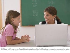 Teacher providing one-on-one literacy instruction to a student using a laptop in a classroom.