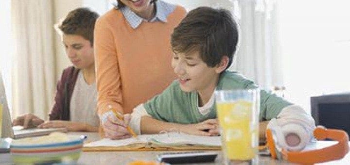 A woman helps two boys with schoolwork at a table.