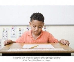 A young boy with dark curly hair sits at a desk with a piece of paper and a pencil.