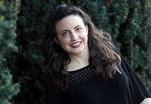 Nina G, a comedian and activist, smiles outdoors with trees in the background.