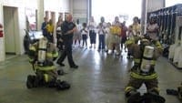 Firefighters race to put on protective gear for a group of middle school students during a fire station tour.