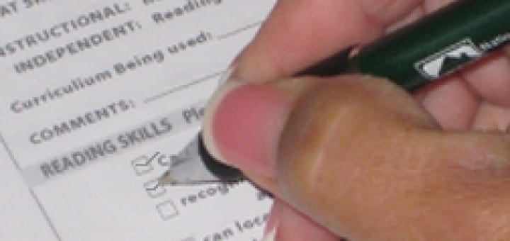 Hand holding a pen to mark progress on an educational reading skills assessment report.