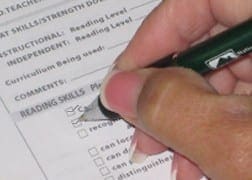 Hand holding a pen to mark progress on an educational reading skills assessment report.