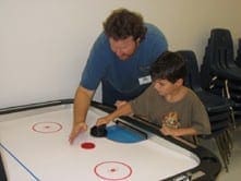 Camp counselor playing air hockey with a young camper to build confidence and social engagement.