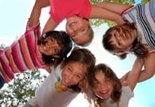 Diverse group of children huddled together in a circle with their arms around each other to signify social connection.