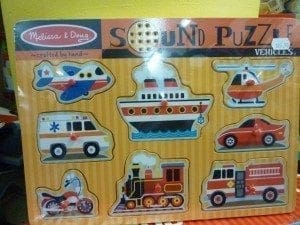 Sound puzzle featuring wooden vehicle cutouts including a plane, ship, ambulance, helicopter, car, motorcycle, train, and fire truck.