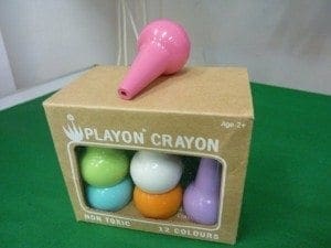 A pink crayon shaped like a microphone rests on a cardboard box of Playon Crayons.