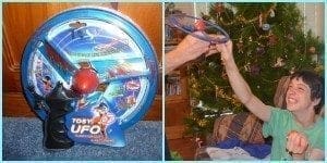 Boy smiles while reaching for a toy UFO in front of a Christmas tree.