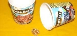 Two Ben & Jerry's ice cream cups and a walnut on a yellow surface.