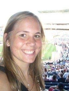 Emily Ruzic smiles at a baseball game with a crowd in the background.