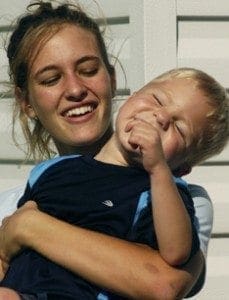 Robin DeVoe smiles while holding a laughing young boy with special needs.