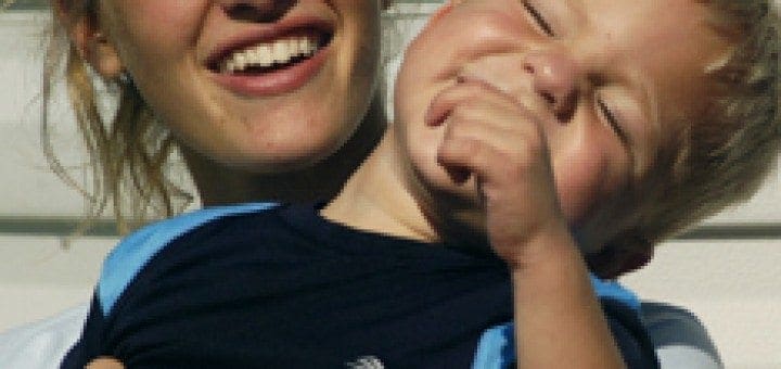 Robin DeVoe smiles while holding a laughing young boy with special needs.