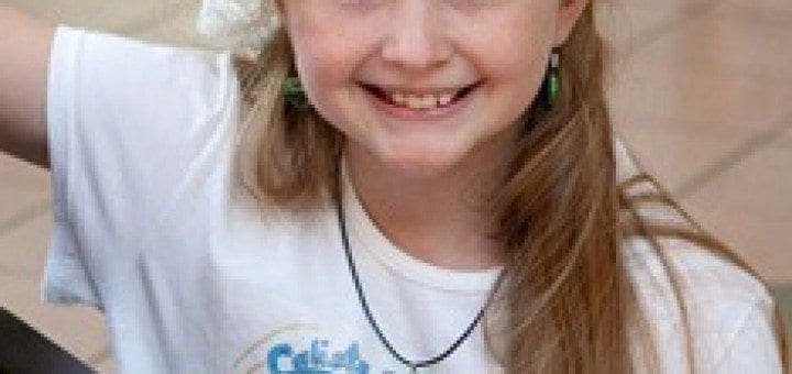 Calista smiles while wearing a white beret, white shirt, and green earrings.