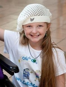 Calista smiles while wearing a white beret, white shirt, and green earrings.