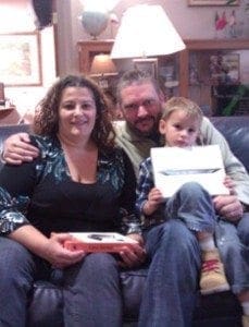 A smiling family sits on a couch, holding an iPad.