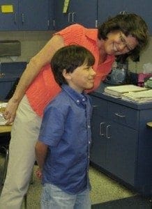 Mrs. Scordino smiles down at a young boy in a classroom.