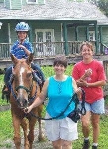 Cindy Economou poses with a child on a horse and another woman.
