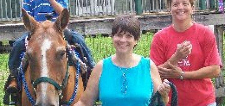 Cindy Economou poses with a child on a horse and another woman.