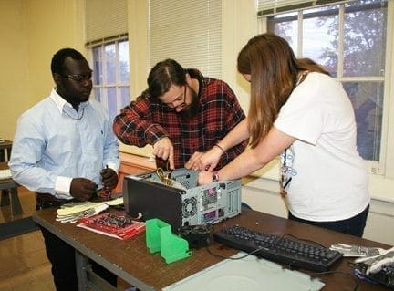 Three people work on disassembling a computer at a lab table.
