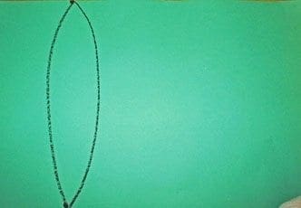 A black crayon draws a large oval on a green background.