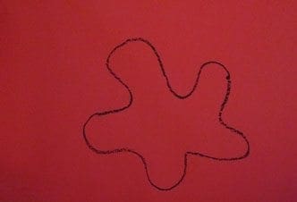 A black crayon drawing of a blob shape on red paper.