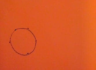 A circle is drawn with crayon on orange paper.