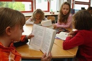 Four students sit at a table reading a book.
