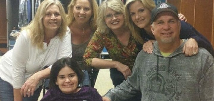Garth Brooks poses with Nicole in a wheelchair and four other women in a dressing room.