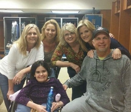 Garth Brooks poses with Nicole in a wheelchair and four other women in a dressing room.